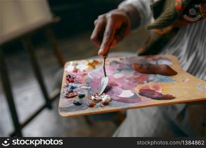 Male painter holds brush and colorful paints on palette, art studio. Artist draws at his workplace. Painter holds brush and colorful paints on palette