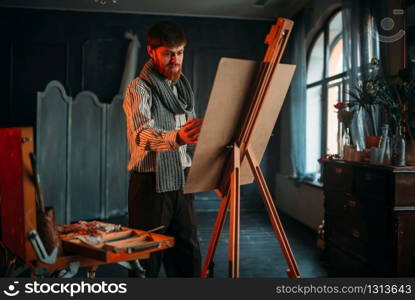 Male painter with brush in hand in front of easel. Oil paint, paintbrush drawing. Male painter with brush in front of easel