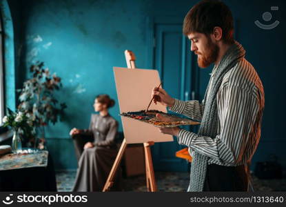 Male painter with palette and brush in hand paints womans portrait on easel. Oil paint, paintbrush drawing