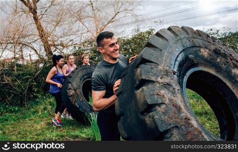 Male participant in an obstacle course turning truck wheel with partners in background. Participant in an obstacle course turning wheel