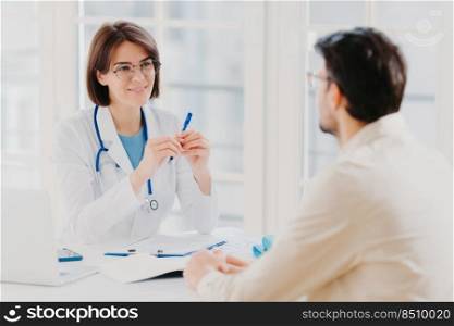 Male patient visits doctor at clinic, tells about his problems, talk about illness. Attentive female doctor writes down notes in medical history, makes prescriptions, listens to patients health issues