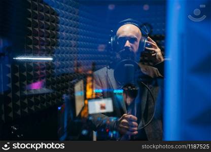 Male performer in headphones songs in audio recording studio. Musician listens composition, professional music mixing