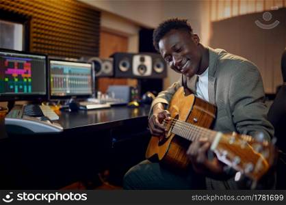 Male performer with guitar, recording studio interior on background. Synthesizer and audio mixer, musician workplace, creative process. Male performer with guitar, recording studio