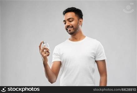 male perfumery, grooming and people concept - happy smiling young indian man with perfume over gray background. happy indian man with perfume over gray background