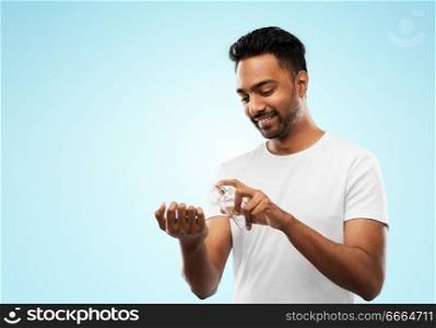 male perfumery, grooming and people concept - happy smiling young indian man spraying perfume to his wrist over blue background. happy indian man with perfume over blue background