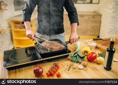 Male person cooking meat in a pan on the kitchen. Man preparing boiled pork on table electric stove