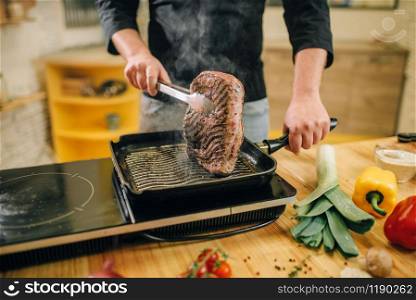 Male person cooking meat in a pan on the kitchen. Man preparing boiled pork on table electric stove. Male person cooking meat in a pan on the kitchen