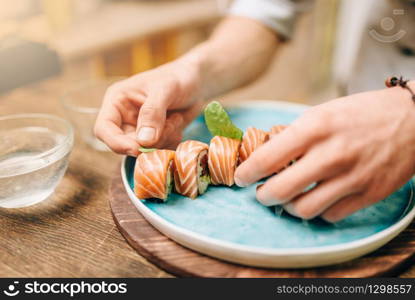 Male person cooking sushi rolls with salmon on wooden table, japanese food preparation process.. Male person cooking sushi rolls, japanese food