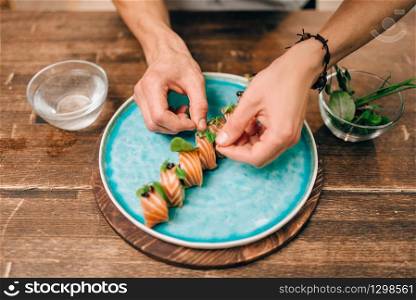 Male person cooking sushi rolls with salmon on wooden table, japanese food preparation process. Traditional asian cuisine, seafood delicious. Male person cooking sushi rolls with salmon