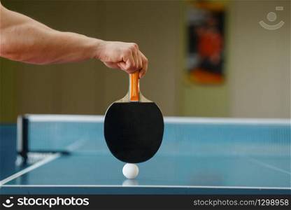 Male person hand with racket and ping pong ball on the table, workout indoors. Man on training in table-tennis club