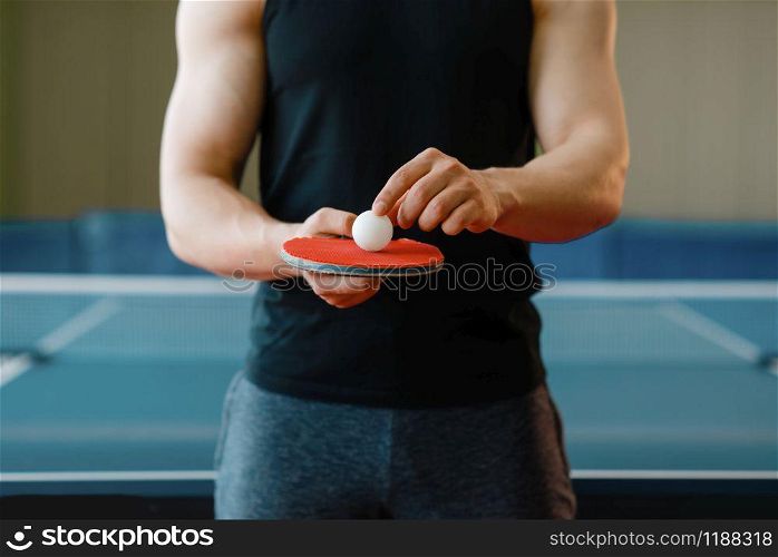 Male person holds racket and ping pong ball on it, workout indoors. Man in sportswear on training in table-tennis club