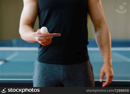 Male person holds racket and ping pong ball on it, workout indoors. Man in sportswear on training in table-tennis club. Male person holds racket and ping pong ball on it
