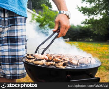 Male person with food tweezers barbequing with lot&rsquo;s of smoke