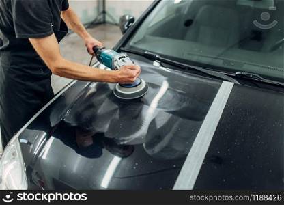 Male person with polishing machine cleans car. Auto detailing on carwash station, restore the paint of vehicle. Male person with polishing machine cleans car