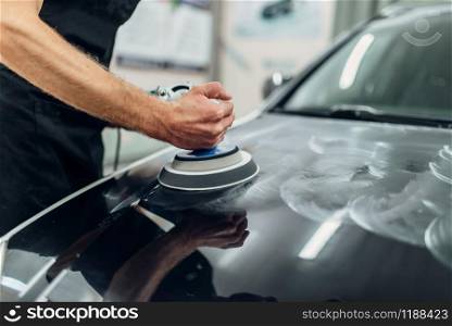 Male person with polishing machine cleans car hood. Auto detailing on carwash service, restore the paint of vehicle. Male person with polishing machine cleans car hood