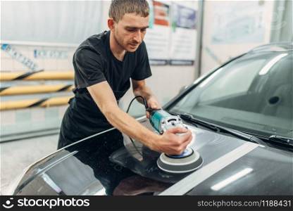 Male person with polishing machine prepares to restore the paint of car. Auto detailing on carwash station. Male person prepares to restore the paint of car