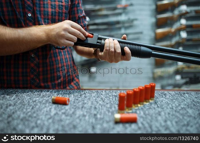 Male person with rifle loads ammo at showcase in gun shop. Euqipment for hunters on stand in weapon store, hunting and sport shooting hobby. Male person with rifle loads ammo in gun shop