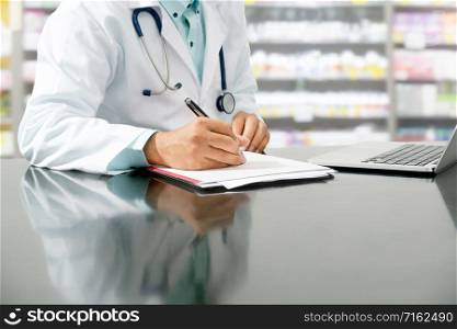 Male pharmacist sitting at table and writing on a document report in pharmacy office. Medical healthcare staff and pharmaceutical service.