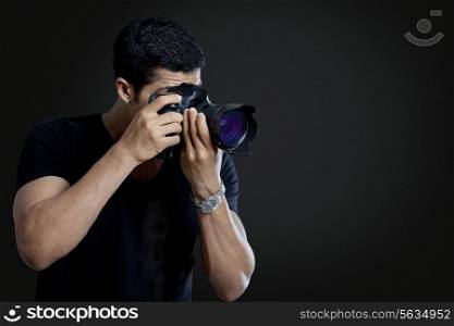 Male photographer taking photograph against black background