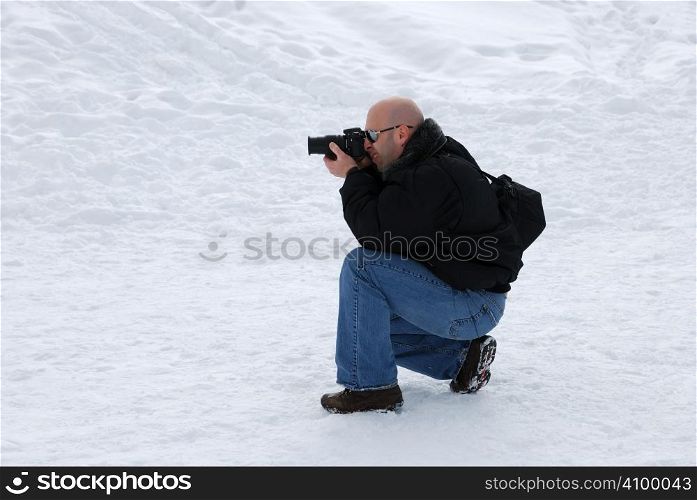 Male photographer with camera taking pictures in snow