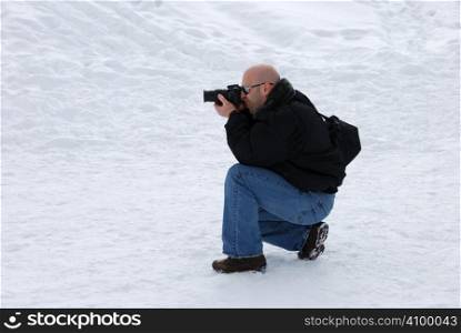 Male photographer with camera taking pictures in snow