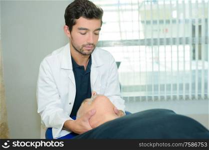 male physiotherapist giving head massage a senior patient in clinic