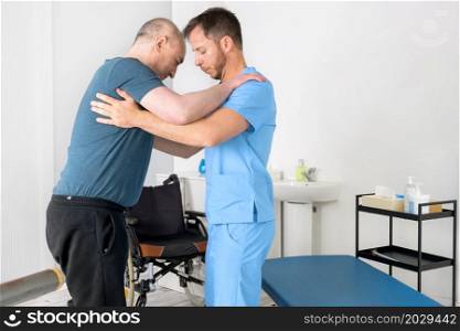 Male Physiotherapist helping a patient with a disability who uses a wheelchair, to get up at rehabilitation hospital. High quality photo.. Male Physiotherapist helping a patient with a disability who uses a wheelchair, to get up at rehabilitation hospital.