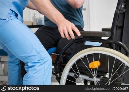 Male Physiotherapist helping a patient with a disability who uses a wheelchair to get up at rehabilitation hospital. High quality photo.. Male Physiotherapist helping a patient with a disability who uses a wheelchair to get up at rehabilitation hospital.