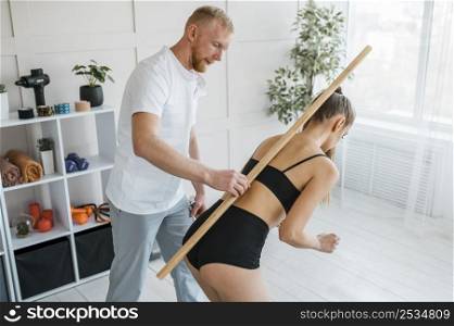 male physiotherapist helping female patient with treatment wooden stick