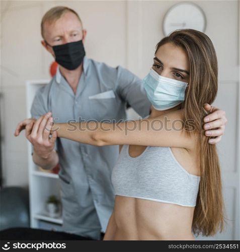 male physiotherapist wearing medical mask during therapy session with woman