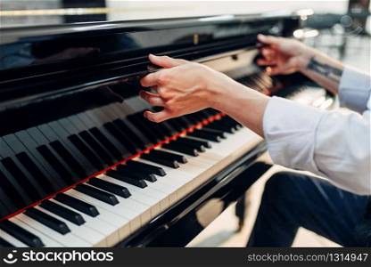 Male pianist opens the keyboard lid of the black grand piano. Musician prepares to performance on the royale, classical musical instrument. Pianist opens the keyboard lid of grand piano