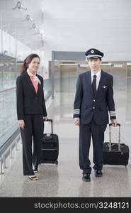 Male pilot and a female cabin crew walking and carrying their luggage in the corridor of an airport