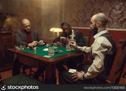 Male player cheating in poker at gaming table, casino. Games of chance addiction, risk, gambling house. Men leisures with whiskey and cigars. Male player cheating in poker