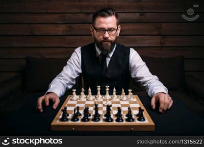 Male player in glasses sitting against the chess board with the pieces set. Strategy game concept. Male player against chess board with pieces set