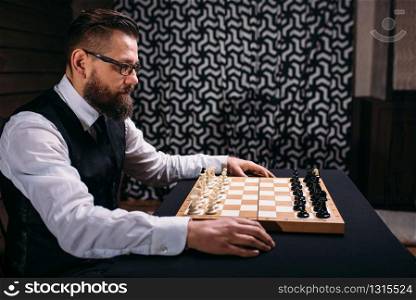Male player in glasses sitting against the chess board with the pieces set. Strategy game concept. Male player against chess board with pieces set