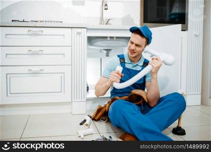 Male plumber in uniform listerns to the drain pipe in the kitchen, humor. Handywoman with toolbag repair sink, sanitary equipment service at home. Male plumber listerns to the drain pipe, humor
