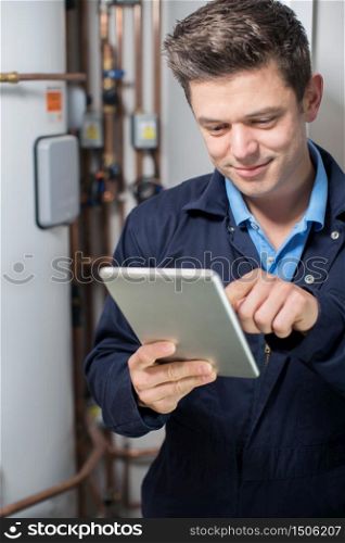 Male Plumber Working On Central Heating Boiler Using Digital Tablet