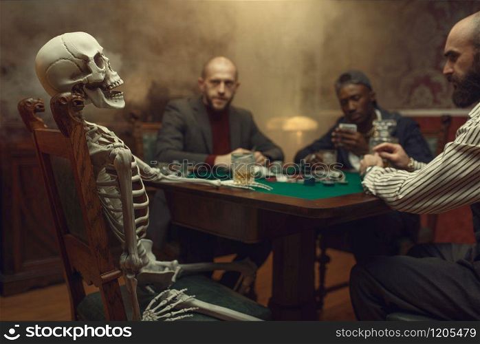 Male poker players and skeleton at gaming table with green cloth, fun, casino. Games of chance addiction, risk, gambling house. Men leisures with whiskey and cigars