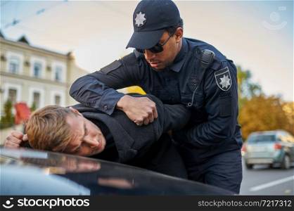Male police officer in sunglasses arrests young man. Policeman in uniform protect the law, registration of an offense. Cop works on city street, order and justice control. Police officer in sunglasses arrests young man