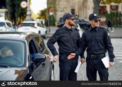Male police officer takes a bribe from a female driver. Policeman in uniform breaks the law, registration of an offense. Corrupt cop works on city street, bad order and justice control, corruption. Police officer takes a bribe from a female driver