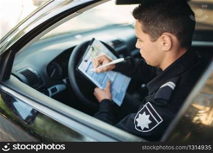 Male policeman in uniform sitting in car and writes a fine. Law protection, car traffic inspector, safety control job. Male policeman sitting in car and writes a fine
