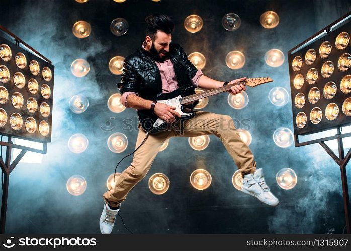 Male pop star with electro guitar on the stage with the decorations of lights. Music entertainment