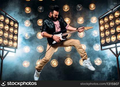 Male pop star with electro guitar on the stage with the decorations of lights. Music entertainment