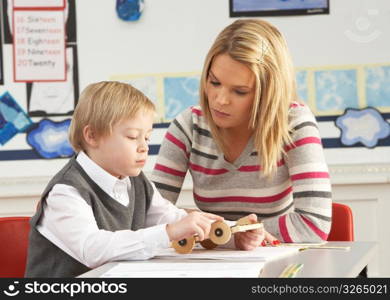 Male Primary School Pupil And Teacher Working At Desk In Classroom