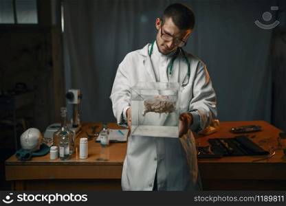 Male psychiatrist in lab coat holds container with the human brain, mental hospital. Doctor in clinic for the mentally ill