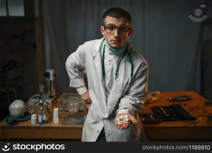 Male psychiatrist in lab coat shows sedative pills, mental hospital. Doctor in clinic for the mentally ill