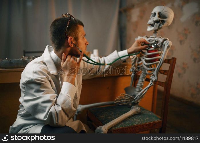 Male psychiatrist with stethoscope listening the skeleton, mental hospital. Doctor in clinic for the mentally ill
