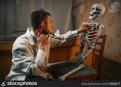 Male psychiatrist with stethoscope listening the skeleton, mental hospital. Doctor in clinic for the mentally ill
