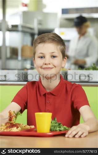 Male Pupil Sitting At Table In School Cafeteria Eating Lunch