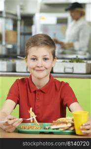 Male Pupil Sitting At Table In School Cafeteria Eating Unhealthy Lunch